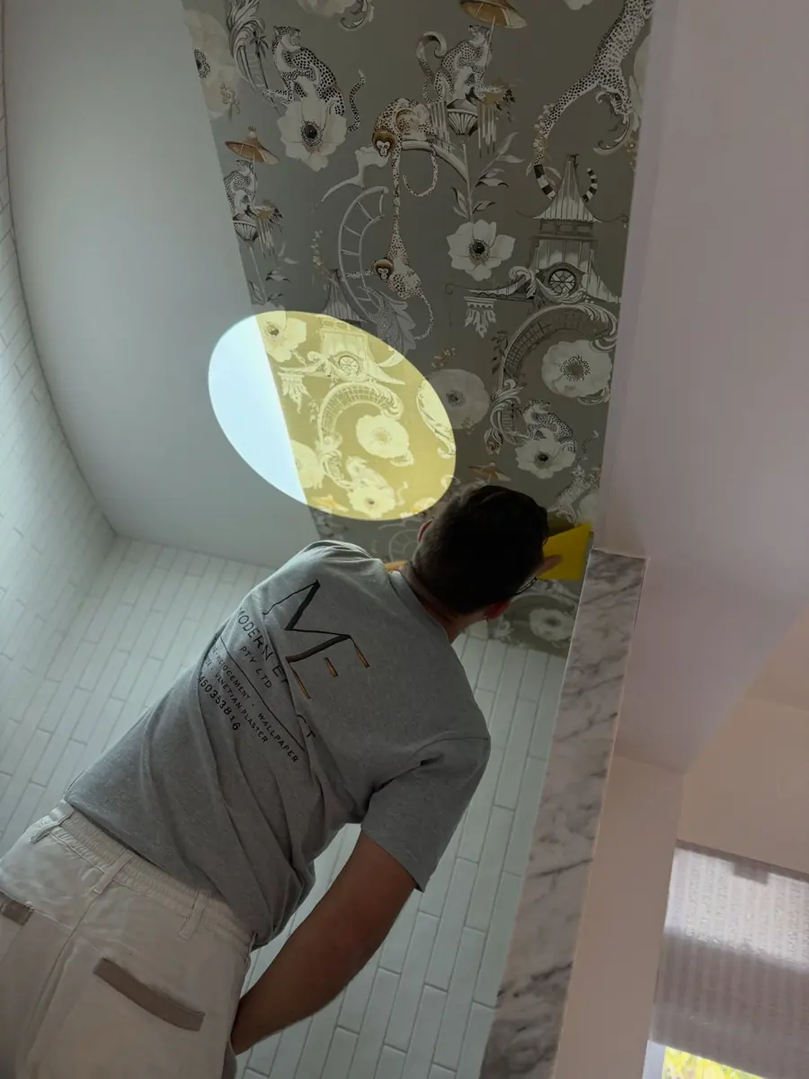 Wallpaper installer smoothing a patterned paper onto a bathroom ceiling